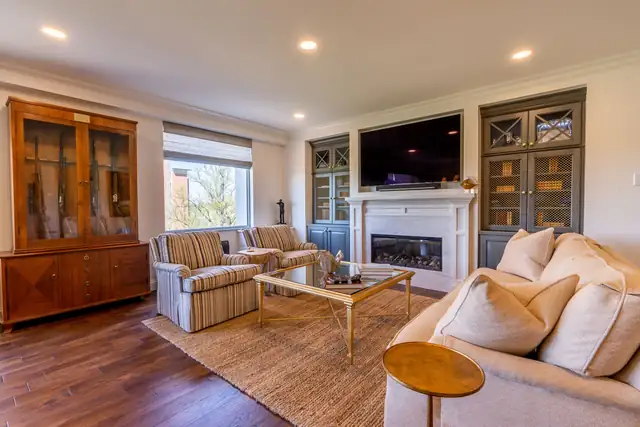 Finished basement with long lit bar, swivel stools, wood-clad columns and stacked stone fireplace wall