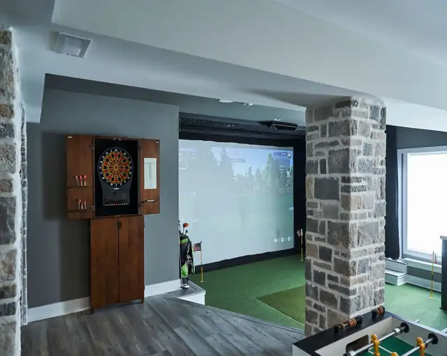 Basement remodel for a golf enthusiast with indoor golf simulator, stone-clad column, dartboard cabinet and wood-look floor