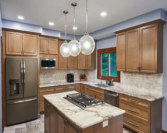 Kitchen with stained wood cabinets, a granite island with a gas cooktop, three glass globe pendants and a stone tile backsplash