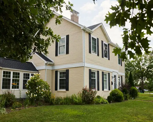 Two-story home with yellow siding and black shutters after a second-story addition that added three bedrooms