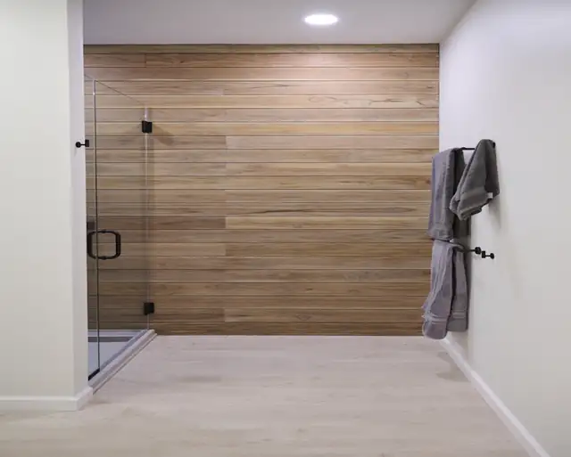 Minimalist bathroom with teak plank accent wall, frameless glass shower and black hardware