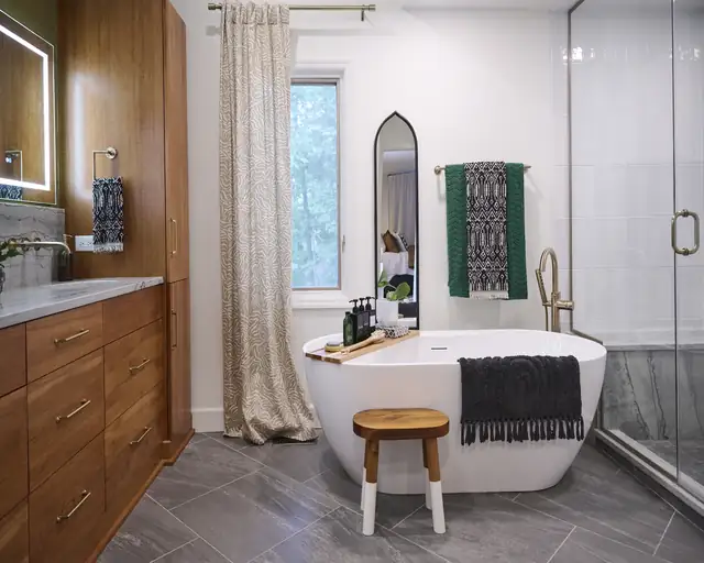 Modern bathroom with freestanding soaking tub, wood bath stool, dark plank floor tile and matte black faucet