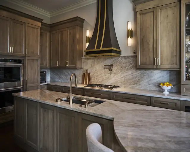 Kitchen with dark stained cabinets, a black and brass range hood and a curved granite peninsula