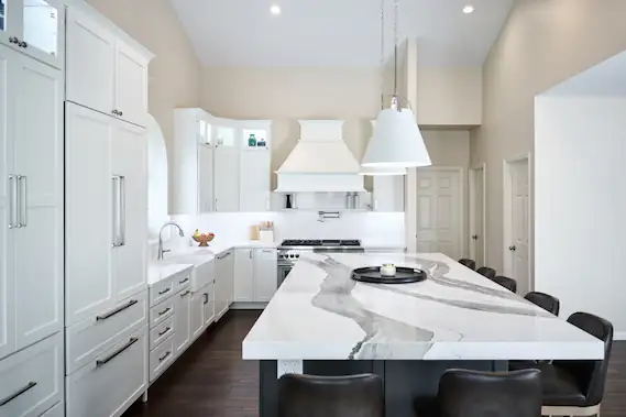 Bright kitchen remodel with vaulted ceiling, white cabinets, white range hood and bold veined island with dark base
