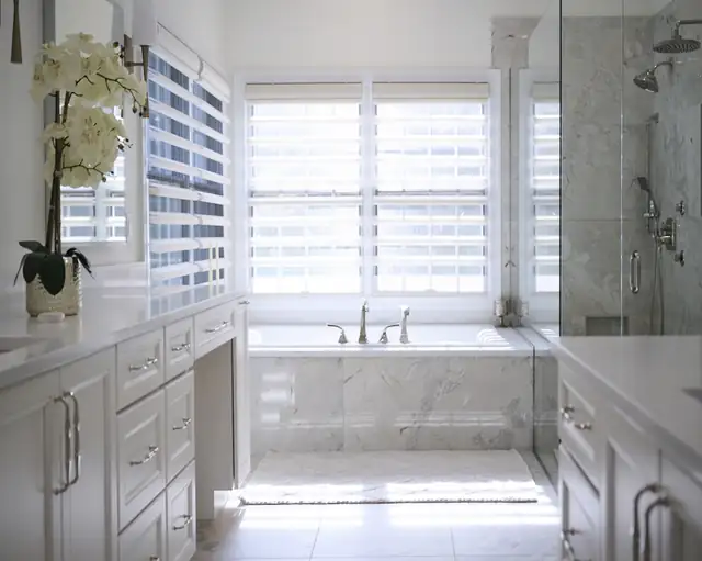 Ballwin primary bathroom remodel with Italian quartzite floor and shower, deep soaking tub under a window and white vanity cabinets