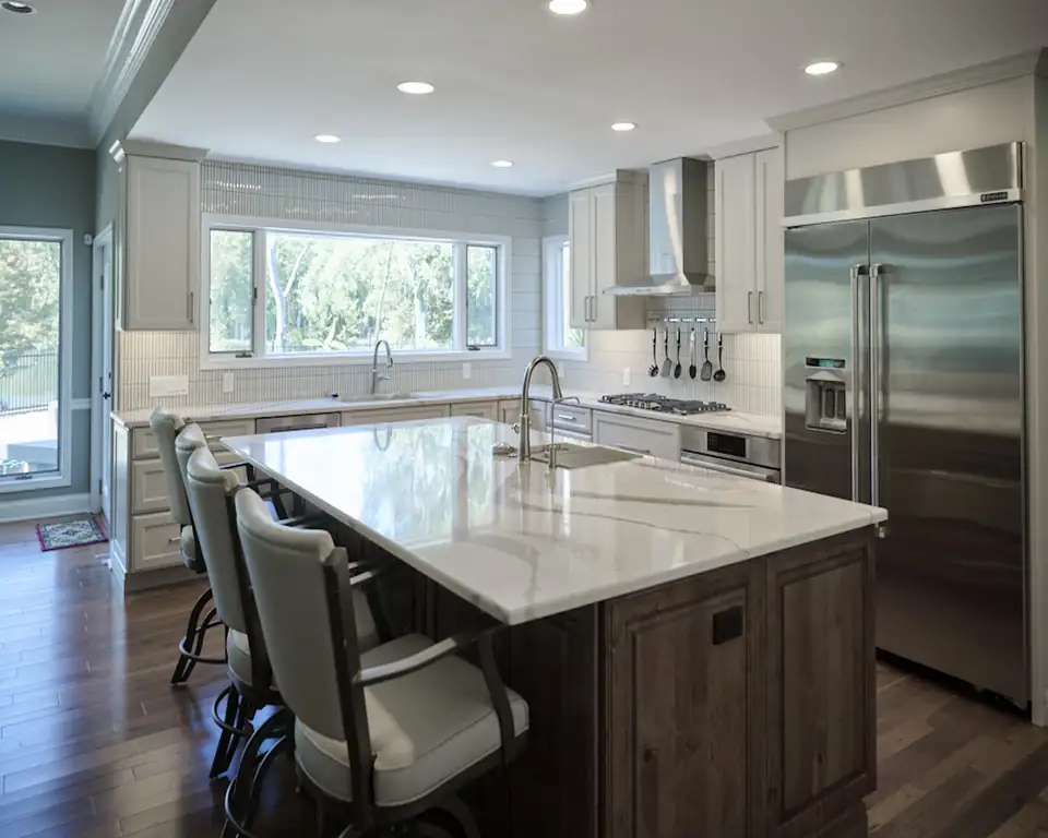 Kitchen remodeling St. Charles: open-concept kitchen with light shaker cabinets, stained wood island with seating, veined counters and stainless built-in refrigerator