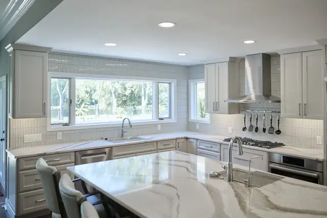 St. Charles open-concept kitchen with veined quartz island, vertical tile backsplash wrapping the windows and gray shaker cabinets