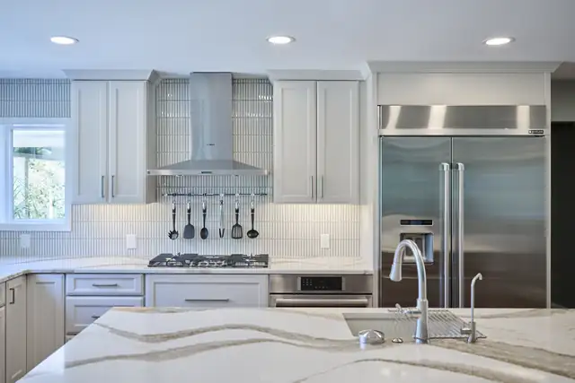 St. Charles kitchen by Aptitude Design & Build with white shaker cabinets, a veined quartz island, a stainless range hood and a built-in refrigerator